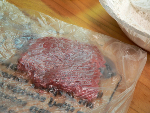 13_Chicken-Fried-Steak_steak-in-plastic-wrap Place the steak on a cutting board and cover with plastic wrap.
